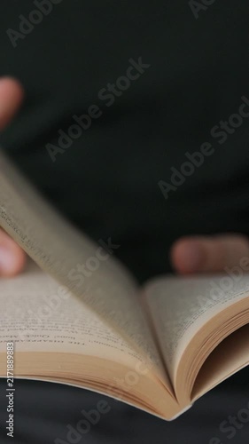 Vertical video. Man is lifestyle sitting on couch in cozy room reading favorite book. Man opens the book and turns the pages of the book.