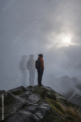 Mountaineer stands resolute on a foggy ridge, surrounded by shifting silhouettes guiding the way forward