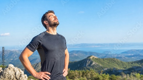 Athletic Man Resting And Breathing Deeply On Mountain Peak Under Clear Blue Sky, Concept Of Wellness And Outdoor Fitness