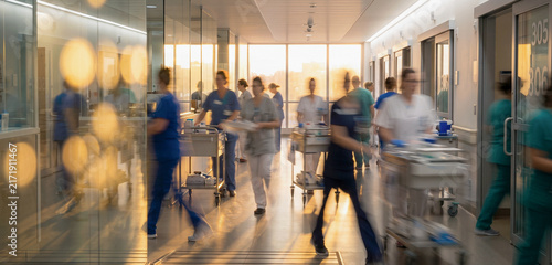 A busy hospital hallway during sunset, with medical staff in scrubs moving quickly. The atmosphere reflects a sense of urgency and care.