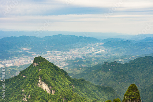 Mountain range overlooking valley and town in landscape of Tianmen forest national park in in Zhangjiajie China with cloudy overcast sky and green lush foliage during summer vacations travel trip