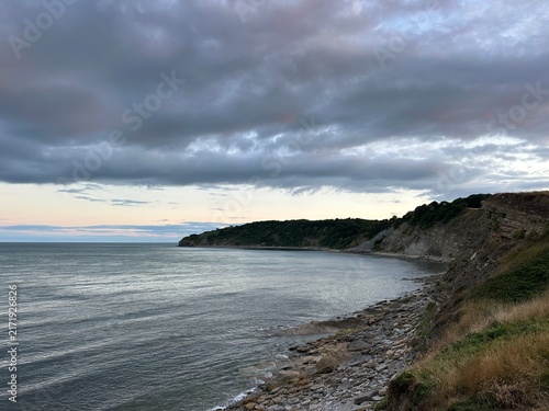 Rocky coastline and calm Atlantic Ocean under cloudy sky near Swanage, England, United Kingdom, July 2025
