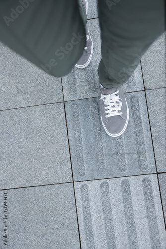Quadro su tela POV of legs walking in sneakers in the city tactile paving