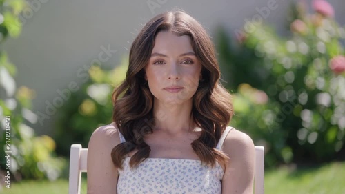 Beautiful young caucasian woman taking a deep breath and sighing with relief while sitting outside in sunny green summer garden

