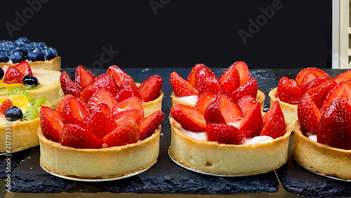 Fresh strawberry tarts and fruit pastries displayed in a cafe showcase.