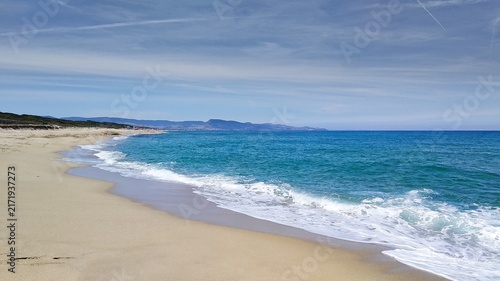 A very long, empty sandy beach with blue waves in Sardinia, near Castelsardo (Italy).