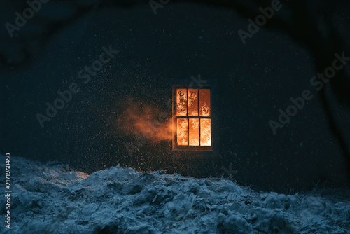 Dark building exterior with glowing orange window and falling snow