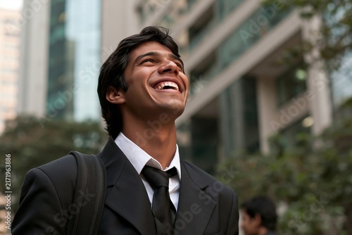 Smiling young businessman looking up while standing outdoors near modern office buildings