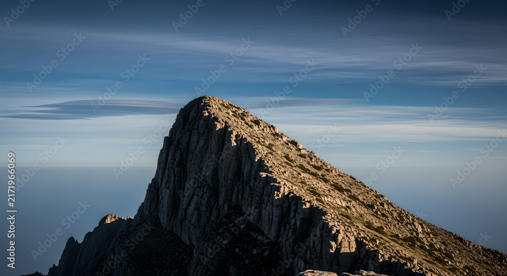 Fototapeta premium Striking rocky mountain peak under a clear blue sky, illuminated by golden sunlight, emphasizing the dramatic and awe-inspiring beauty of a high-altitude wilderness