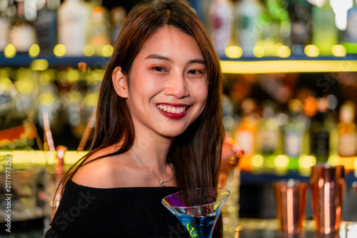 Fotografía A beautiful young Asian woman in a black off-shoulder top holding a bright blue cocktail holds the blue cocktail up beside her face and smiles in a flattering beauty close-up