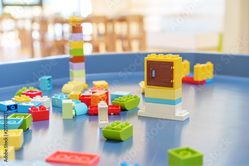 Colorful plastic building blocks scattered on blue play table in bright classroom, early childhood education and creative play concept.