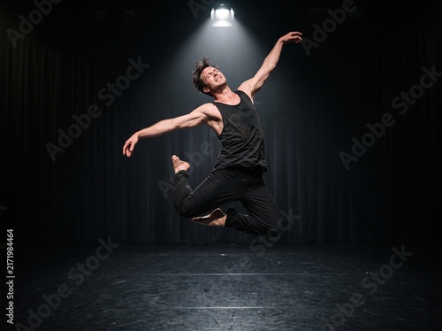 Handsome male ballet dancer leaping in the air on dark stage under spotlight