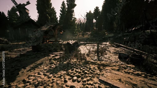 An eerie, deserted settlement features dilapidated buildings and scattered stone pathways, illuminated by the warm glow of the setting sun through dense trees.