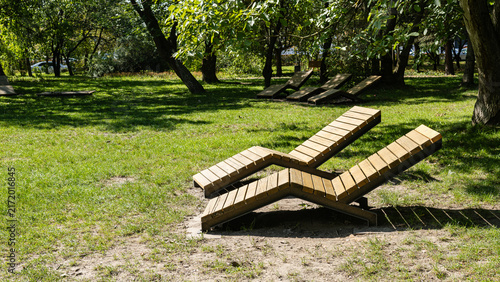 Fotografía Wooden sun loungers on green grass in sunny public park