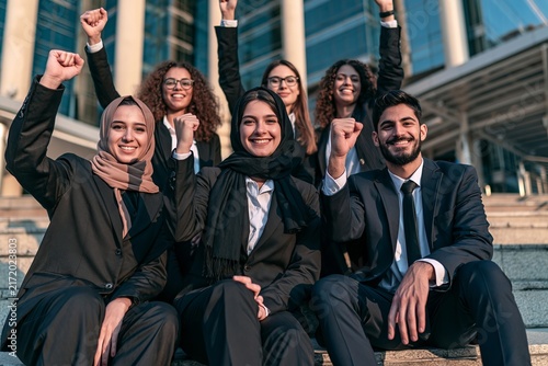 Diverse group of happy business professionals celebrating success with raised fists outside office