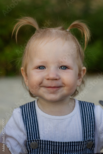 Adorable toddler with blue eyes and pigtails smiles sweetly outdoors