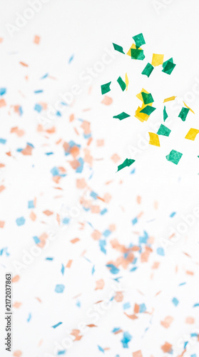 Scattered confetti in blue, orange, yellow and green against a white background, creating a festive and celebratory atmosphere, perfect for party or event themes