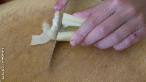 Hands slicing green bell pepper on wooden cutting board. Close-up shot.
