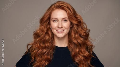 Beautiful Woman with Voluminous Red Curly Hair Smiling Against Studio Background