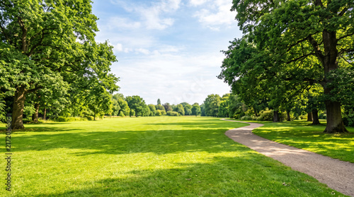 Scenic View of Green Public Park with Gravel Pathway, Lawn, and Lush Green Trees Under Sunny Sky