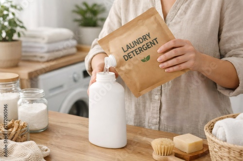 Person choosing sustainable laundry practices by refilling a reusable bottle with liquid detergent from an environmentally friendly craft paper pouch in a bright laundry room