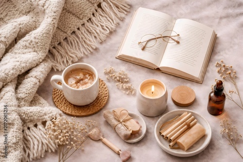 Flat lay composition showcasing a relaxing environment with a cup of coffee, an open book, a burning candle, and natural spa elements creating a serene atmosphere