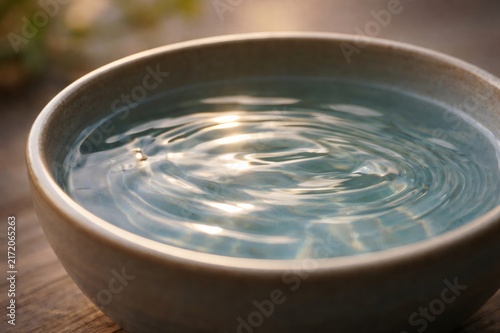 Clean water forming concentric ripples in a ceramic bowl, golden sunlight reflecting on the surface to create a serene, meditative scene of purity and calmness
