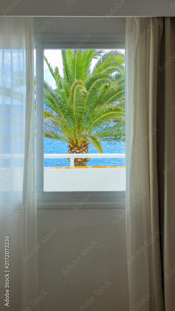 Fototapeta premium Hotel window overlooking the sea with palm tree