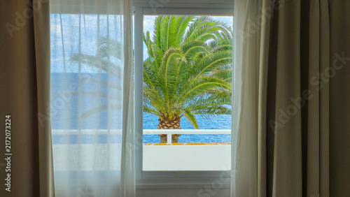Hotel window overlooking the sea with palm tree