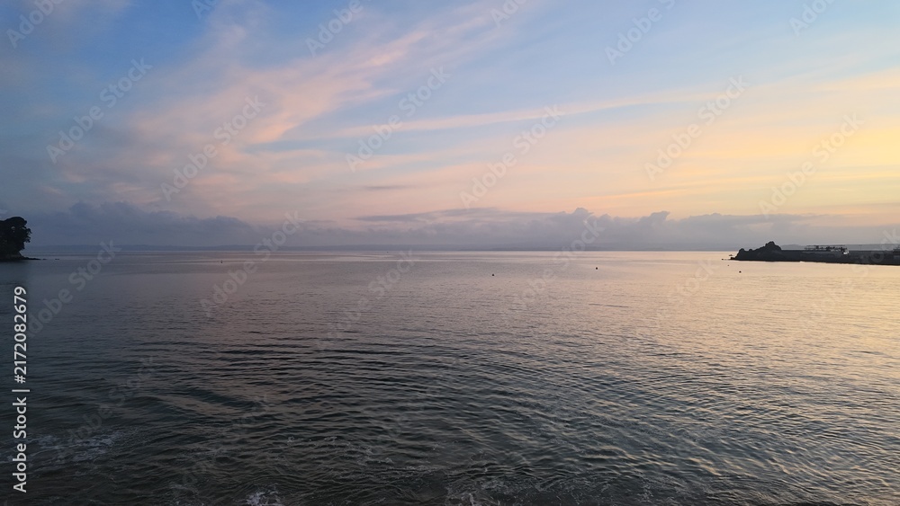 Obraz premium Pastel sunrise over the calm sea and distant coastline in Brittany, France.