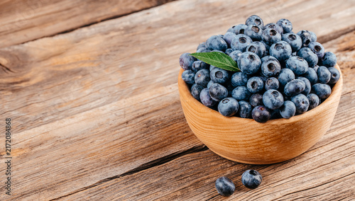 Quadro su tela Fresh blueberries in a wooden bowl on rustic wooden table, with a few berries sc