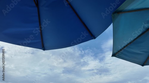 Low angle view of blue beach umbrellas set against a cloudy blue sky