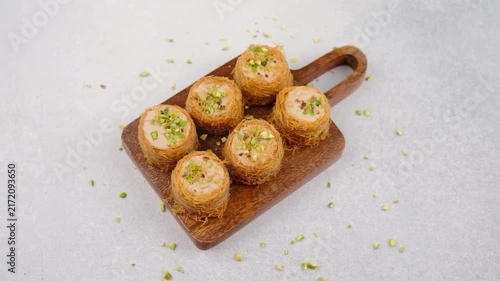 Sweet rolled baklava pastries with chopped pistachios on a wooden board