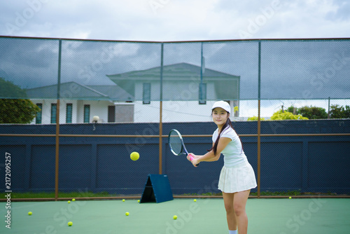 Принти на полотні Confident young Asian woman in white tennis outfit practices backhand swing on a