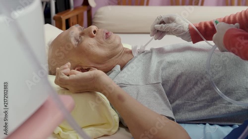 Asian nurse suctions mucus from a tube in the throat of a patient who had a tracheostomy and is recovering at home 