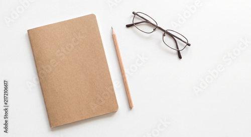 Notebook photo with pencil and reading glasses on clean white minimalist workspace

