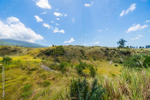 Serene rural landscape featuring lush green grass and rolling hills beneath a clear blue sky. A peaceful nature scene at the Batu Angus tourist area in Bitung, Indonesia.