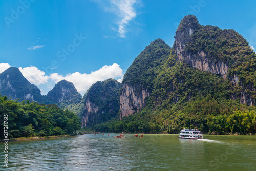 Fotografie Guilin, China, a passenger boat cruises the emerald Li River beneath dramatic ka