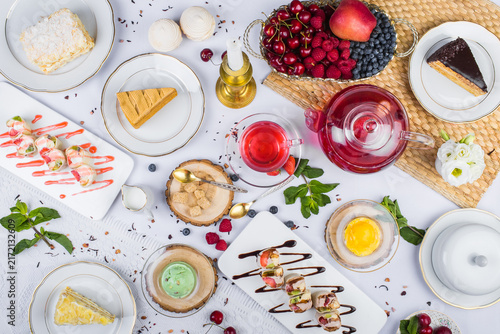 Foto Top-view lavish tea feast featuring sweet pastries, sweet rolls, red berry tea, fresh cherries, and colorful treats on a bright white table