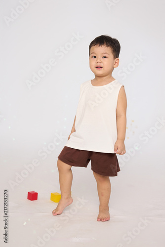 A 3-year-old toddler standing in a basic pose, wearing brown shorts and a white short-sleeved shirt.