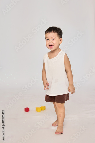 A 3-year-old toddler standing in a basic pose, wearing brown shorts and a white short-sleeved shirt.
