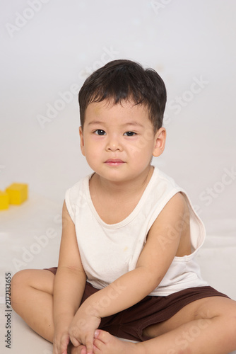 A 3-year-old toddler sitting in a basic pose, wearing brown shorts and a white short-sleeved shirt.