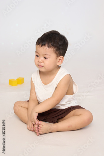 A 3-year-old toddler sitting in a basic pose, wearing brown shorts and a white short-sleeved shirt.