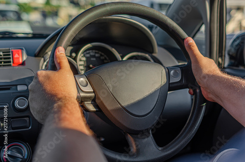 A person holds the steering wheel while driving a car during daylight hours.