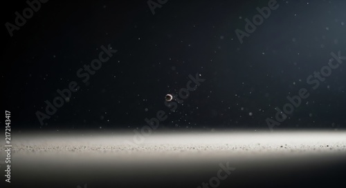 A small, solitary circular floating in a dark, atmospheric space filled with tiny particles, dust, and glowing specks, creating a mysterious, cosmic, and ethereal visual composition