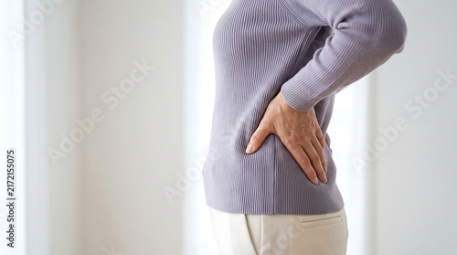 A woman is holding her lower back in pain, indicating discomfort or a medical issue.
