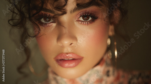 Close-up portrait of a young woman with curly hair and elegant makeup