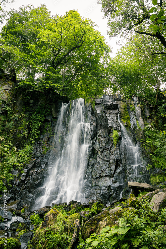 Obraz premium Refreshing Cascade de Vaucoux surrounded by lush forest in the Massif du Sancy, Auvergne, France, representing tranquility, coolness, natural beauty and an escape into nature.