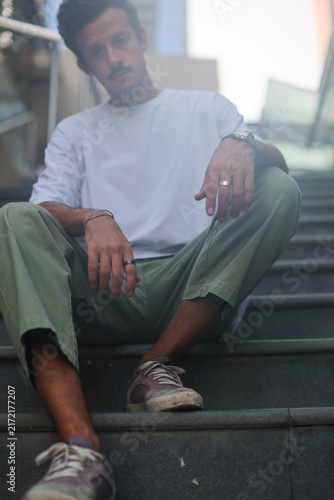 Blank white oversized t-shirt mockup on a young male model sitting on city stairs, urban street style apparel template