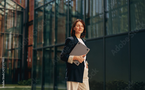 Businesswoman holding a laptop outside a glass office building